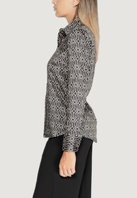 Camicia a maniche lunghe a righe bianche e nere con colletto, texture fluida e taglio dritto, abbinata a pantaloni neri larghi.