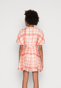 Vestido de manga curta em xadrez nas tonalidades pêssego e branco, apresentando uma cintura ajustada e uma saia rodada, confeccionado em tecido leve com uma textura suave.