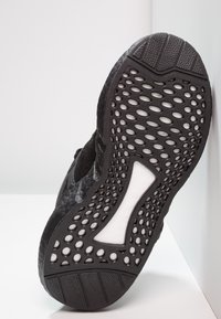 Svart atletisk skosula med texturerat gummi och cirkulära utskärningar. Solid vit accent i mitten. Mjuk övre kant.