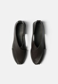 Tamnosmeđe kožne cipele s otvorenim dizajnom, s preklopom sprijeda i glatkom teksturom. Potplat je ravna i minimalistička.