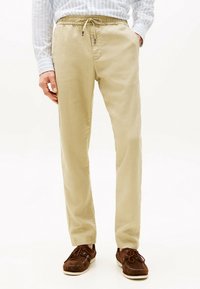 Beige Leinenhose mit elastischem Bund und Kordelzug. Glatte Textur mit lockerer Passform, kombiniert mit braunen Wildlederschuhen im Boot-Stil.
