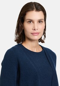 Granatowy sweter z okrągłym dekoltem, miękką teksturą i długimi rękawami. Ma diagonalny szew i subtelne prążkowane akcenty na brzegach.