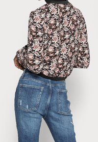 Blumen-Bomberjacke in Schwarz mit rosa und weißen Mustern. Kombiniert mit hochtaillierten, hellblauen, verwaschenen Jeans.