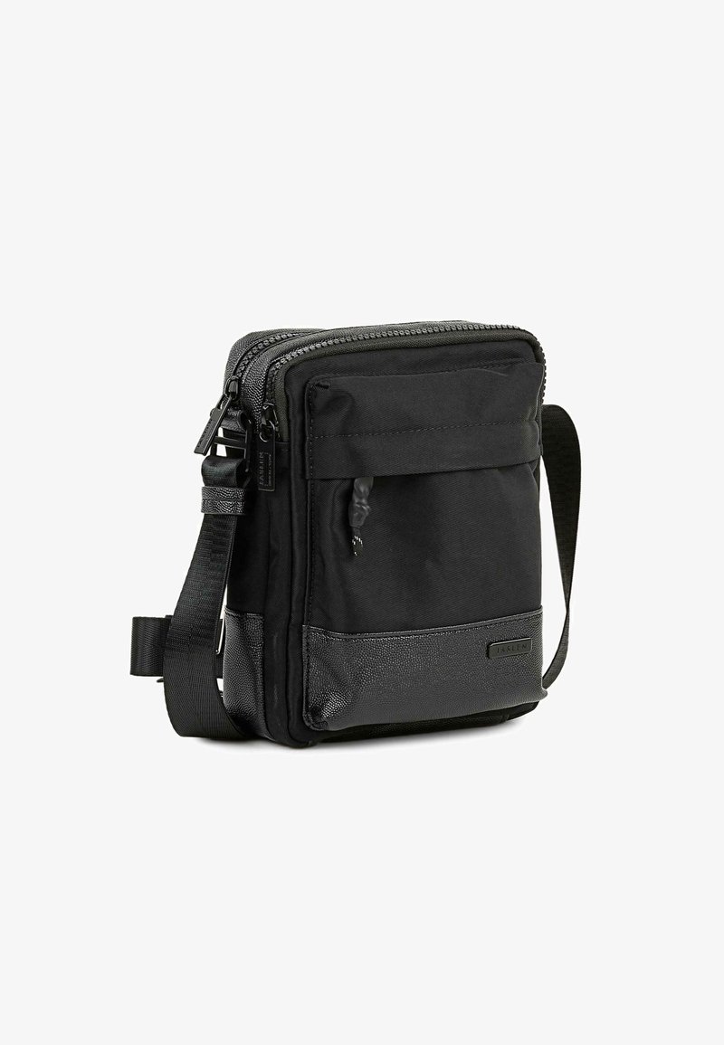 Bolso cruzado negro hecho de tela duradera, con un compartimento principal con cremallera, bolsillo frontal y panel inferior texturizado. Correa ajustable.