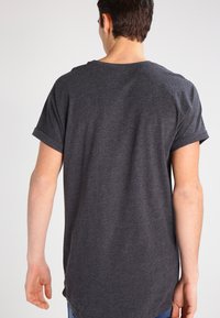Camiseta de manga corta color gris oscuro con escote redondeado y puños enrollados, que presenta un dobladillo trasero más largo y una textura de tela suave.
