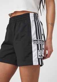 Black athletic shorts featuring white side stripes, an elastic waistband, and an embroidered Adidas logo on the left side pocket.