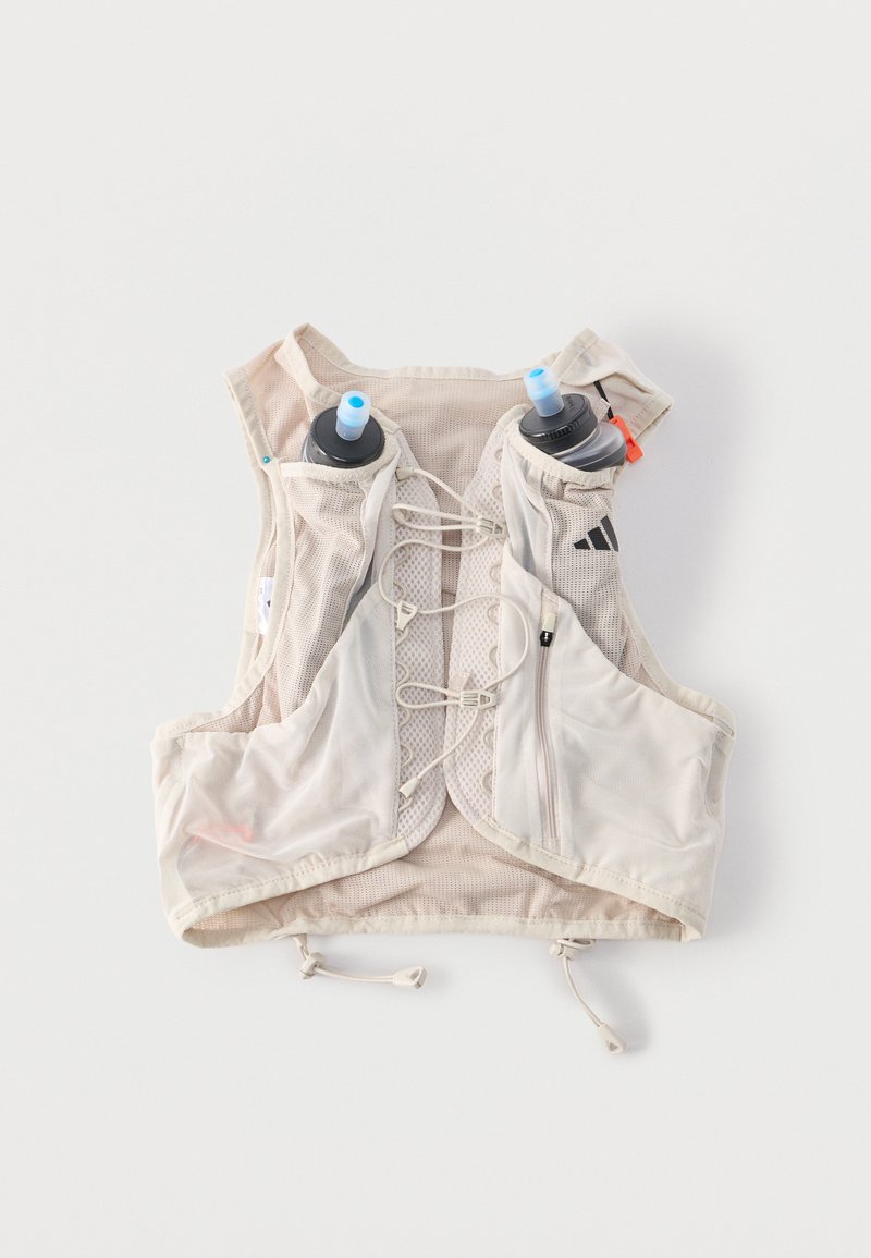 Ανοιχτό μπεζ τρέχον γιλέκο με ρυθμιζόμενα κορδόνια μπροστά, δύο μπροστινές τσέπες για μπουκάλια νερού που κρατούν μπουκάλια με μπλε στόμια και μια μπροστινή τσέπη με φερμουάρ.