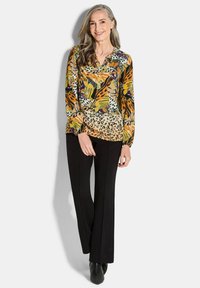 Langärmlige Bluse mit einer Mischung aus bunten Blumen- und Tiermotiven, kombiniert mit schwarzen Hosen und figurbetonten schwarzen Stiefeletten.