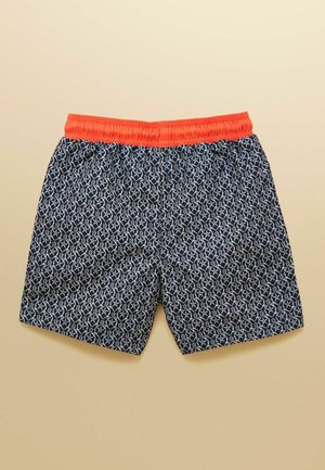 Pantalones cortos azul marino con patrón geométrico blanco y cintura elástica naranja brillante, extendidos sobre un fondo beige.