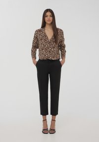 Blusa con stampa leopardata e scollo a V profondo, maniche lunghe, abbinata a pantaloni neri a sigaretta e sandali neri con cinturini.