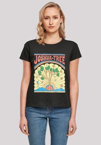 Black t-shirt featuring a colorful graphic design with a yellow tree, rainbow, and stars, labeled "JOSHUA TREE" in bold red letters.