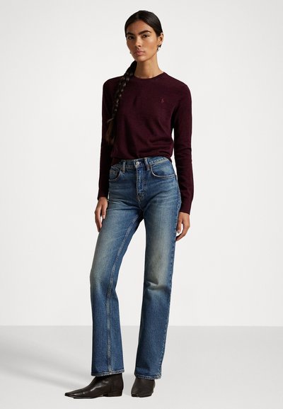 Chemise à manches longues bordeaux associée à un jean bleu taille haute, avec une coupe droite et une décoloration subtile. Des bottines noires à la cheville complètent le look.