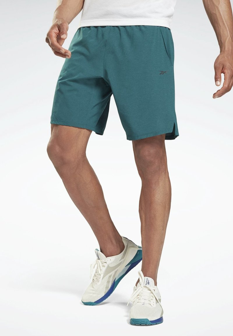Shorts de sport bleu sarcelle en matériau doux, dotés d'une taille élastique et de poches latérales. Associés à des baskets blanches et bleu sarcelle.
