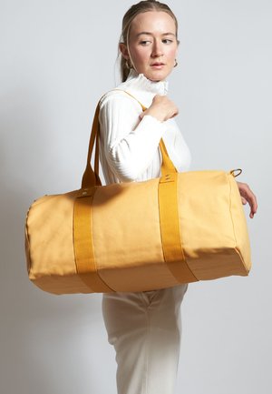 Borsa a tracolla gialla in canvas, dotata di manici robusti e due cinghie orizzontali. Texture liscia con cuciture visibili e dettagli in metallo.