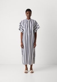 Abito a righe bianco e blu navy con colletto alto, maniche a sbuffo corte e una linea fluida, abbinato a sandali di colore chiaro.