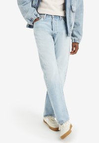 Light blue denim jeans with a straight leg fit, featuring a high waist and subtle distressing. Paired with white sneakers and a light jacket.