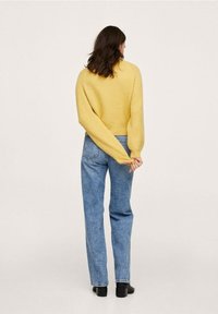 Pull jaune tricoté à manches longues avec une coupe courte, associé à un jean en denim bleu taille haute et des bottines noires.