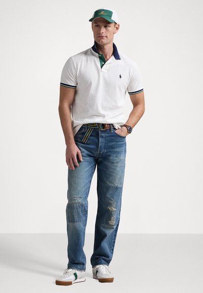 Pikétröja i vitt med grön och marinblå krage, blå jeans med slitna lappar, och vita sneakers med gröna accenter. Avslappnad outfit.