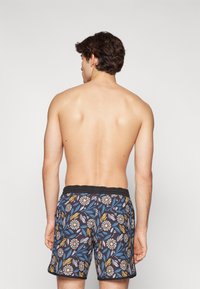 Shorts de bain avec un motif floral bleu et noir, taille élastique, et impression de feuilles et de fleurs en jaune, blanc et bleu.
