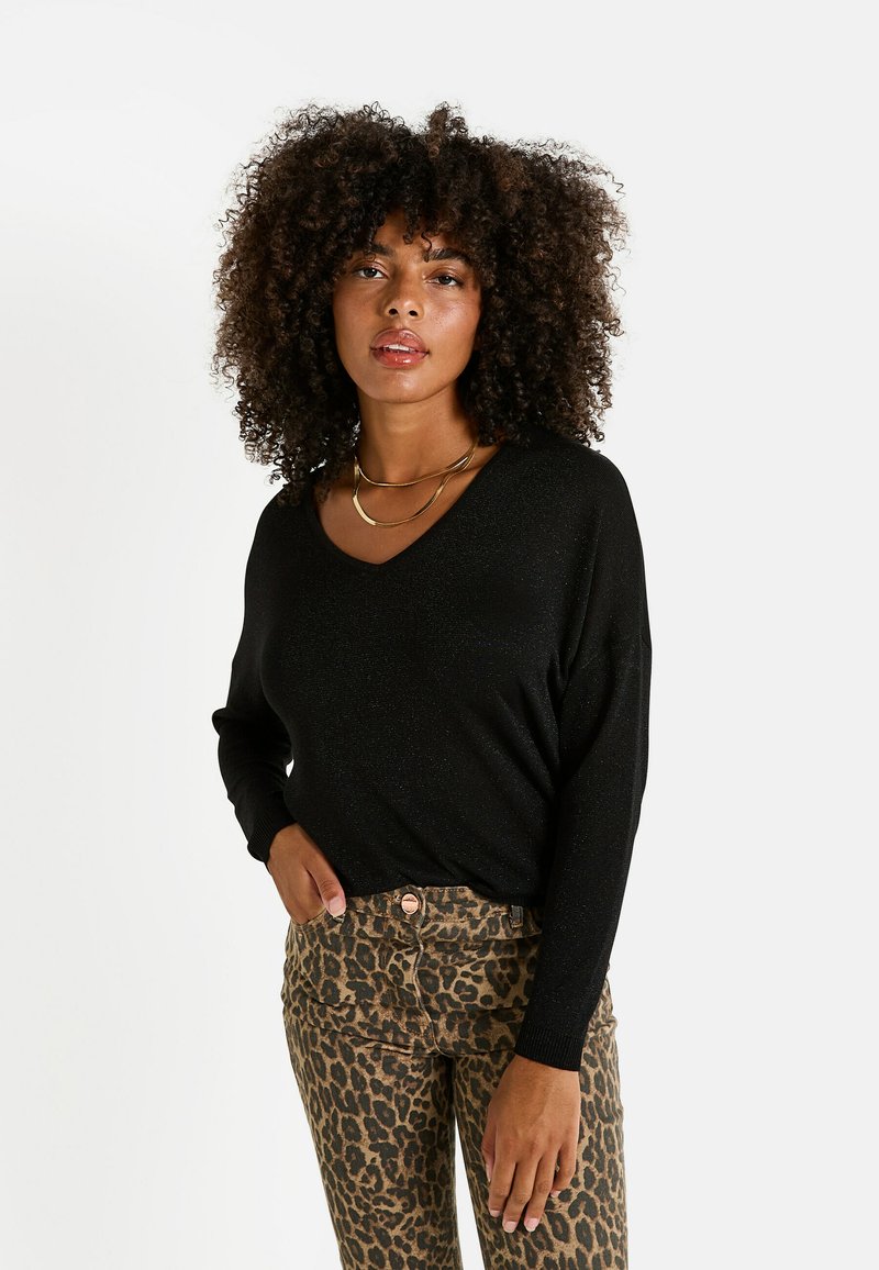 Top negro de manga larga con escote en V, hecho de una tela brillante. Combinado con jeans ajustados de estampado de leopardo con cierre de botón.