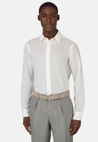 Camicia bianca a maniche lunghe con colletto classico e placket a bottoni, abbinata a pantaloni grigi chiari e una cintura intrecciata beige.