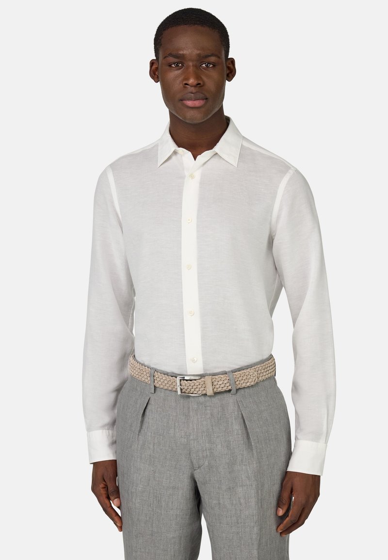 Camicia bianca a maniche lunghe con colletto classico e placket a bottoni, abbinata a pantaloni grigi chiari e una cintura intrecciata beige.