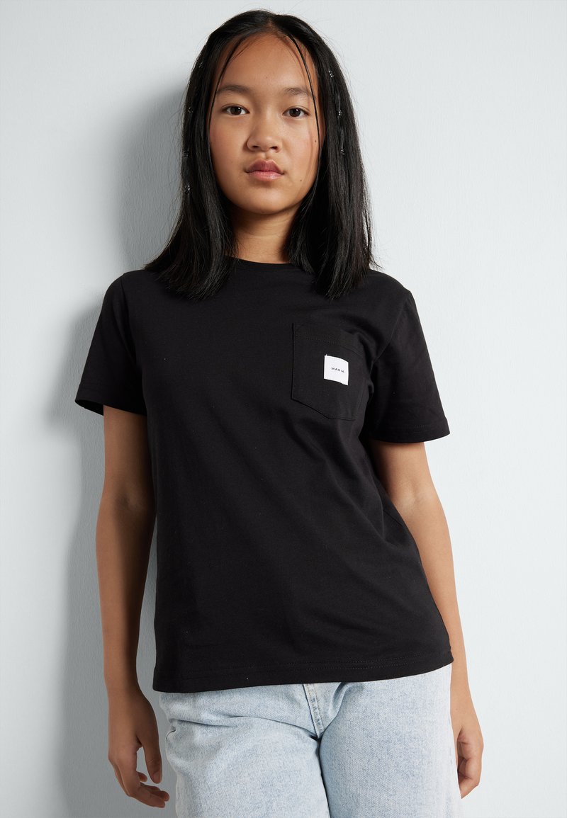 Svart bomull t-skjorte med korte ermer, rund hals og frontlomme. Har en liten hvit etikett på lommen. Brukes med lyseblå jeans.