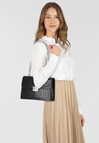 Borsa a tracolla nera con motivo coccodrillo, dotata di una chiusura argentata e di una tracolla a catena, abbinata a una camicia bianca e a una gonna plissettata beige.