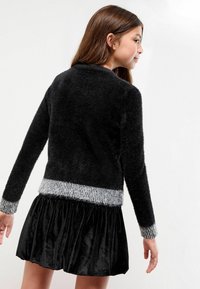 Maglione nero morbidissimo con orlo e polsini a coste grigi, abbinato a una gonna nera in velluto. Design semplice con un contrasto di morbidezza e texture.