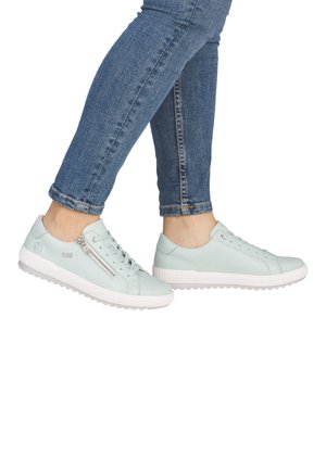 Person wearing light blue leather sneakers with white soles and side zipper, paired with blue skinny jeans against a white background.