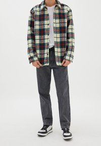 Flanelová košile v krémové barvě s kostkovaným vzorem v zelené, červené a modré, zapínaná na knoflíky, kombinovaná s tmavě šedými džínami a černo-bílými teniskami.