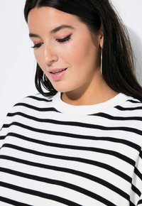 Maglietta a righe bianco e nero con scollatura a girocollo. Il tessuto sembra morbido; presenta un fit rilassato e maniche lunghe. Orecchini a cerchio notevoli.