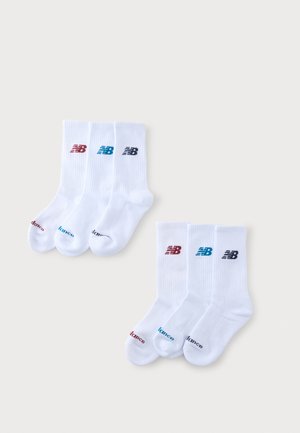 Zes paar witte crew sokken met gekleurde New Balance-logo's in rood, blauw en zwart, getoond op een lichte achtergrond.