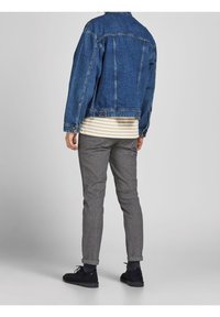 Giacca di jeans blu scuro, camicia a righe grigia sotto, pantaloni grigi con texture e scarpe scure. Presenta bottoni e orli dei pantaloni risvoltati.