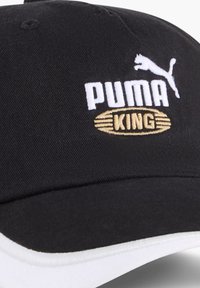Fekete sapka ívelt karimával, fehér hímzett "PUMA" logóval és arany "KING" címkével, textúrált anyagon. Fehér kiegészítő a karimán.