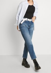 Person wearing light blue open shirt over black tank top, blue jeans with white belt, and black lace-up platform boots.