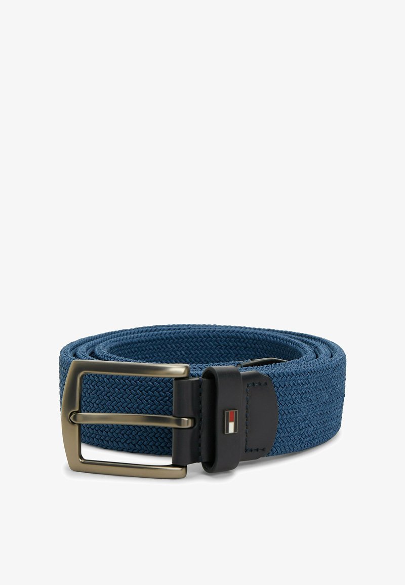 Ceinture en tissu bleu tissé avec boucle en cuir noir et boucle rectangulaire en laiton ancien, posée enroulée sur fond blanc.