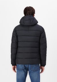 Zwarte pufferjas met een capuchon, voorzien van horizontaal gestikte secties, elastische manchetten en een gladde textuur. G Draag met blauwe spijkerbroeken.