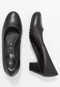 Schwarze Leder-Absatzschuhe mit runder Zehenpartie, niedrigem Blockabsatz und perforiertem Innenfutter für Atmungsaktivität. Markenlogo im Inneren sichtbar.