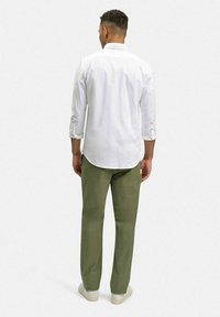 Vit långärmad skjorta med uppvikta ärmar, parat med olivgröna byxor, visad bakifrån. Enkel design, lätt vikt.