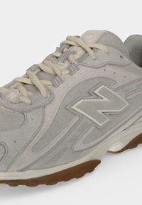 Ανοιχτό γκρι sneaker από σουέτ με κρεμ κορδόνια, υφασμένη σόλα και μεγάλο ραμμένο λογότυπο "N" στο πλάι.
