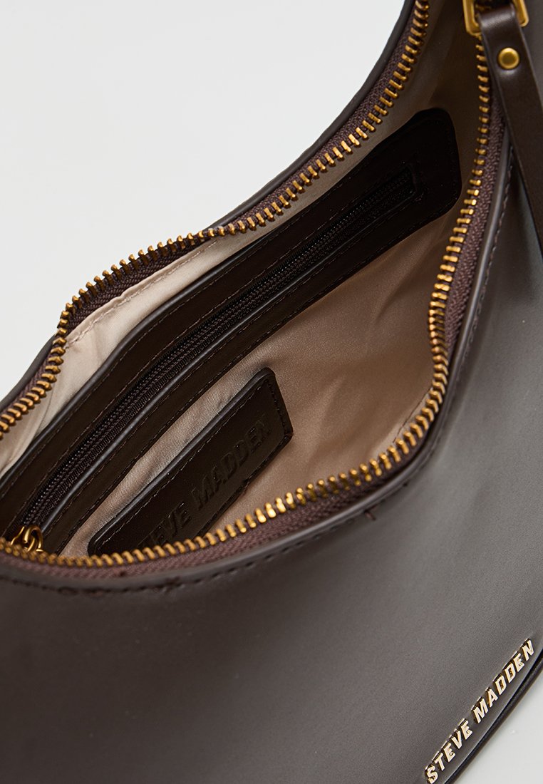 Interno di una borsa in pelle marrone con tasca a zip, fodera in tessuto e dettagli in metallo color oro. Etichetta visibile all'interno della tasca.