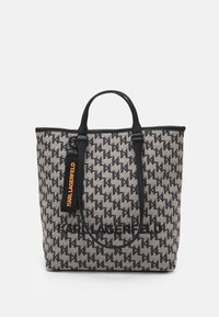 Tote bag in textured gray fabric with a black geometric pattern, featuring black leather handles and a prominent black logo, plus an orange tag.