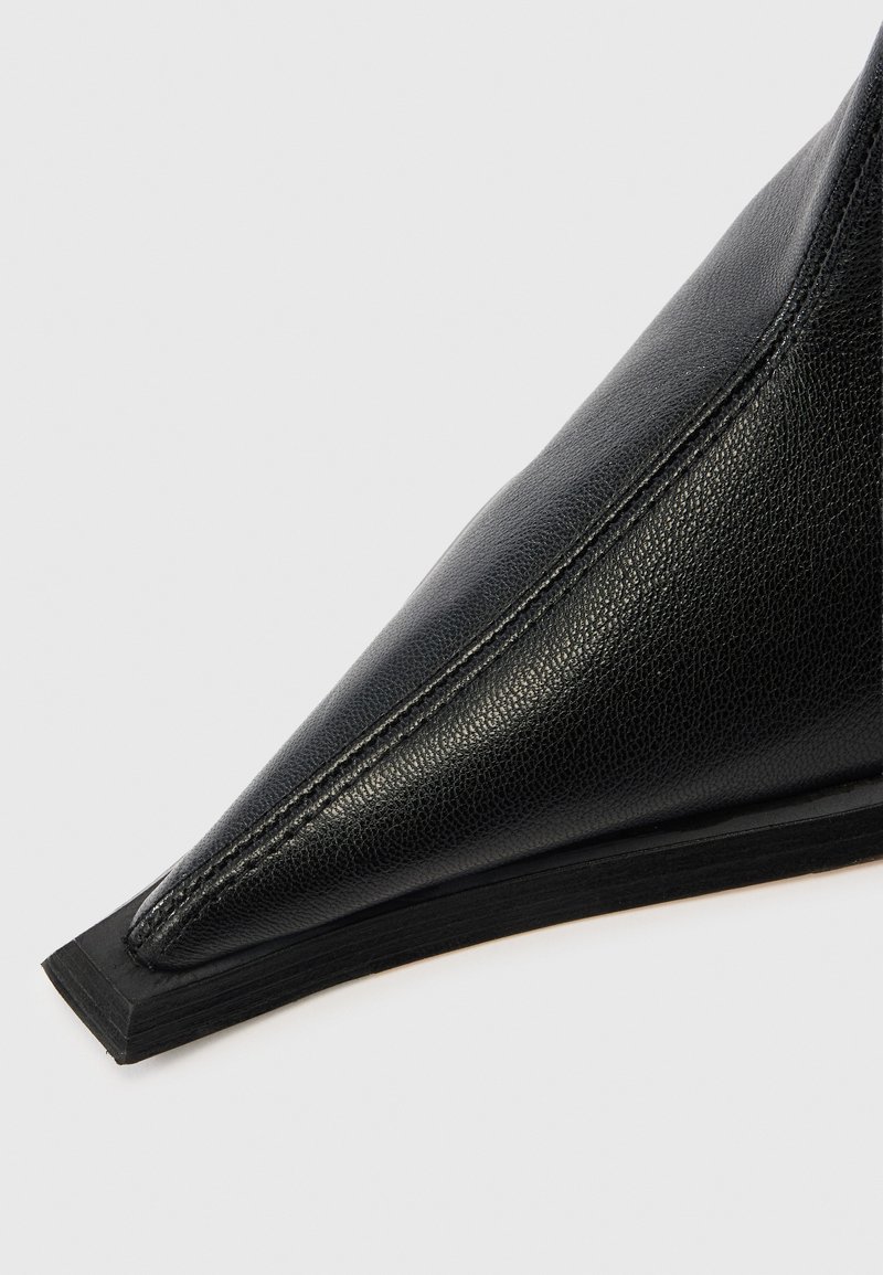 Schwarzer Lederschuh mit spitz zulaufender Spitze, einer strukturierten Oberfläche und einem dezenten Nahtdetail. Die Sohle ist flach mit einem leichten Gummirand.