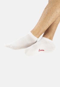 Chaussettes blanches jusqu'à la cheville avec un design en maille. Elles présentent un poignet solide et un logo "Eminence" rouge. Texture lisse, sans motifs.