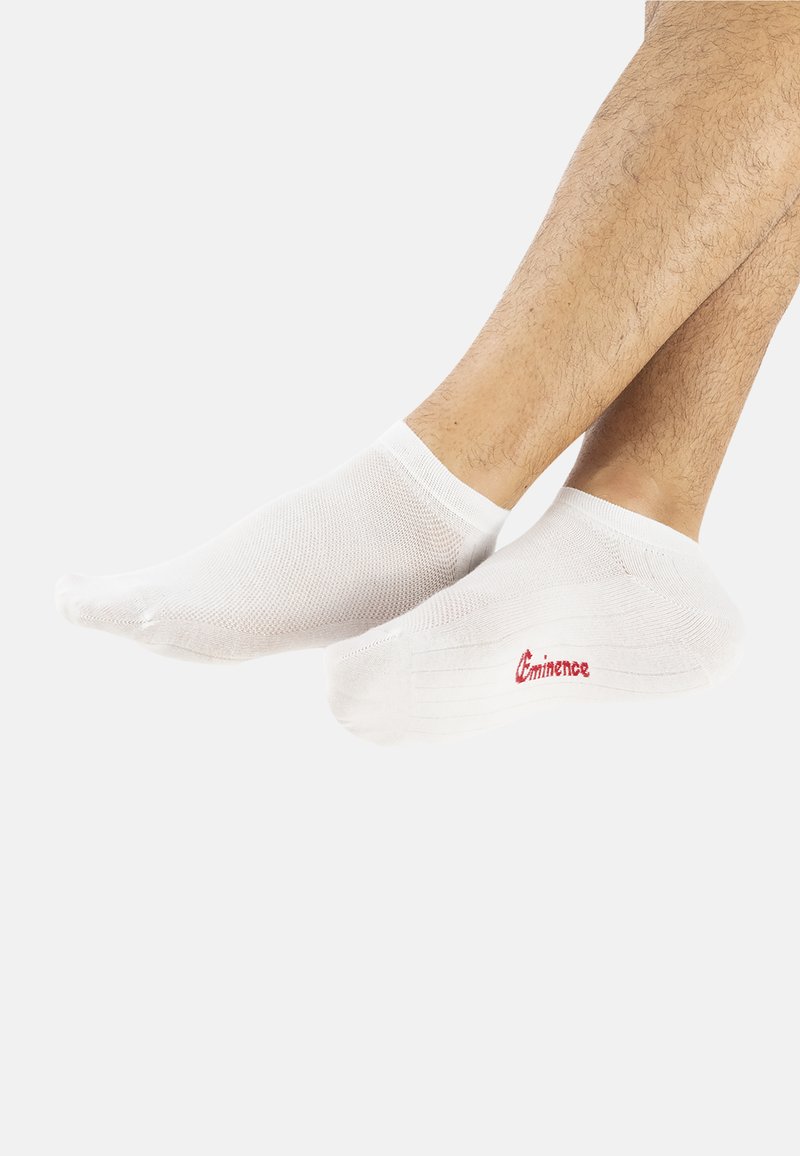 Chaussettes blanches jusqu'à la cheville avec un design en maille. Elles présentent un poignet solide et un logo "Eminence" rouge. Texture lisse, sans motifs.
