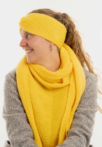 Set di sciarpa e fascia per capelli lavorati a maglia di colore giallo, con una finitura testurizzata. La sciarpa è avvolta attorno al collo, in abbinamento a un maglione grigio.