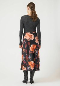 Falda negra con flores grandes naranjas y azules, tela fluida, combinada con una blusa gris de manga larga ajustada y botas negras hasta la rodilla.