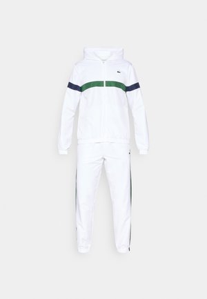 Weißer Trainingsanzug mit grünen und marineblauen Streifen über der Brust und an den Seiten. Verfügt über eine Kapuze und elastische Bündchen. Glatte Stofftextur.