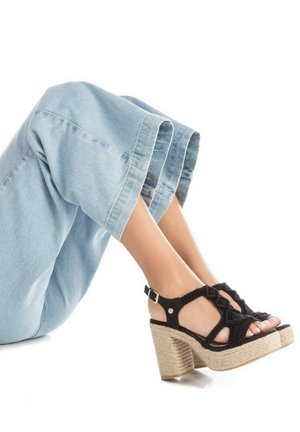 Sandalias negras de tejido con un tacón grueso de yute natural y tira en el tobillo, combinadas con pantalones de mezclilla sueltos de color azul claro.